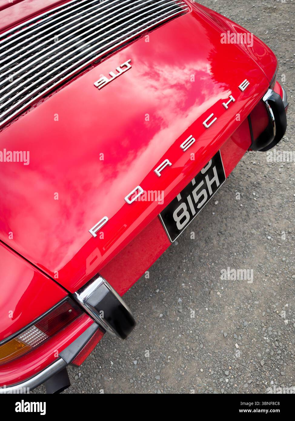 Primo piano del retro della Porsche 911 rossa d'epoca con finitura verniciata lucida esposta su strada ghiaiosa in un ambiente esterno - Immagine stock catturata con smartphone