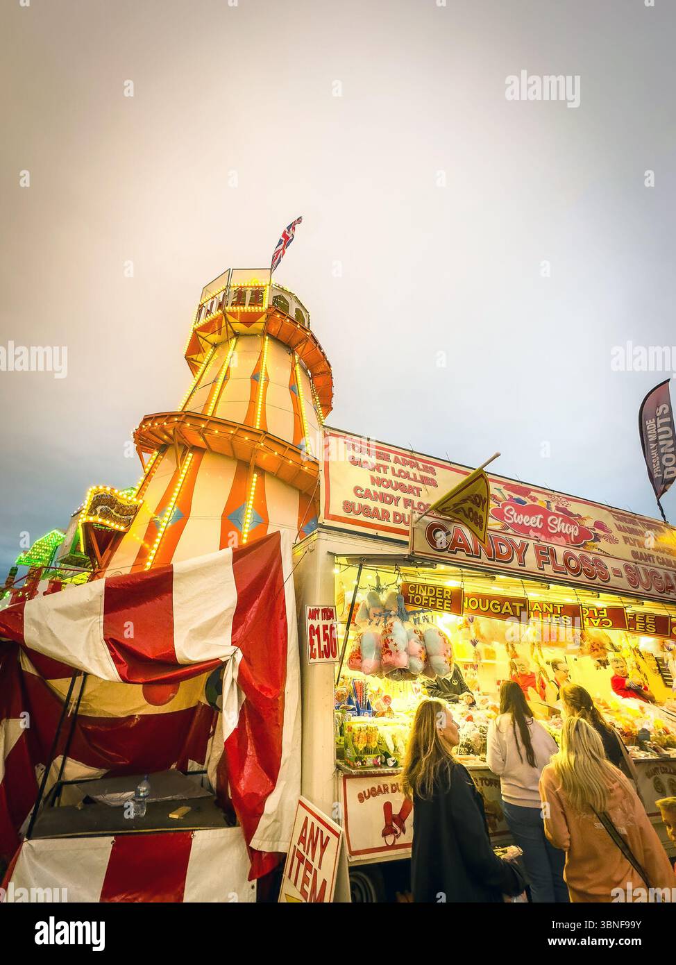Gente alla fiera del divertimento di newcastle con un negozio di caramelle e un giro in elicottero d'epoca durante il crepuscolo, la città di Hoppings ormeggia a newcastle - Immagine stock catturata con smartphone