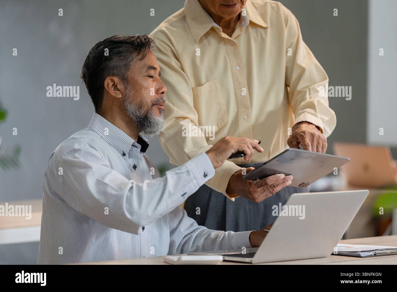 Tecnologia e assistenza. Un uomo anziano che mostra un tablet a un consulente mentre discute delle strategie aziendali. Foto Stock