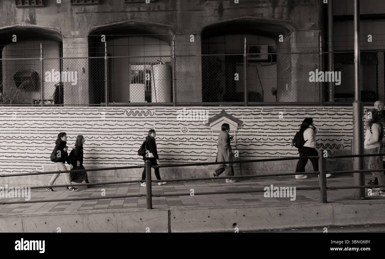 Sottopassaggio monocromatico di Tokyo Street con pareti d'arte a motivi geometrici e persone in movimento Foto Stock