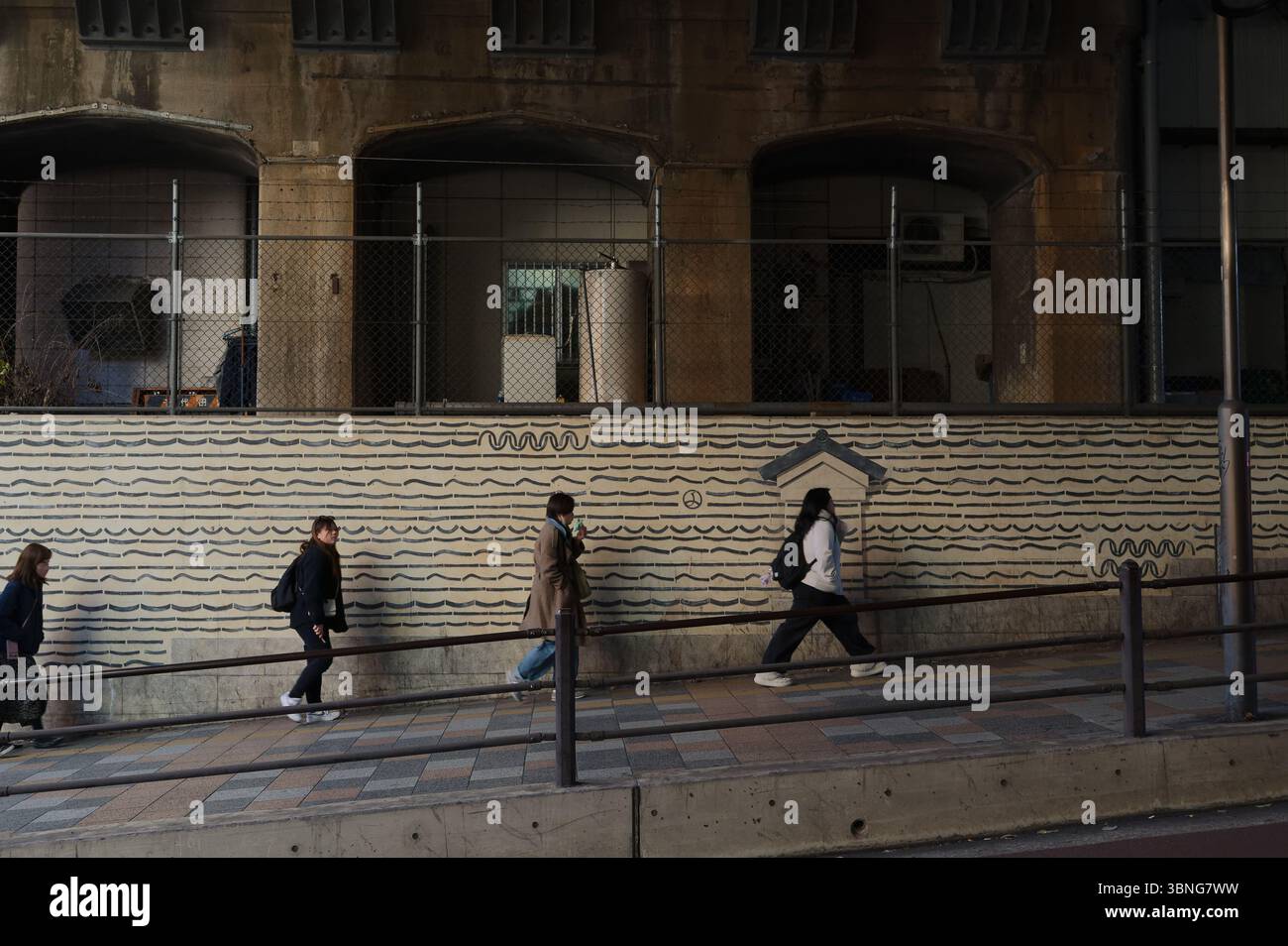 Le persone passano davanti a un muro a motivi geometrici sotto un sottopassaggio di Tokyo poco illuminato Foto Stock