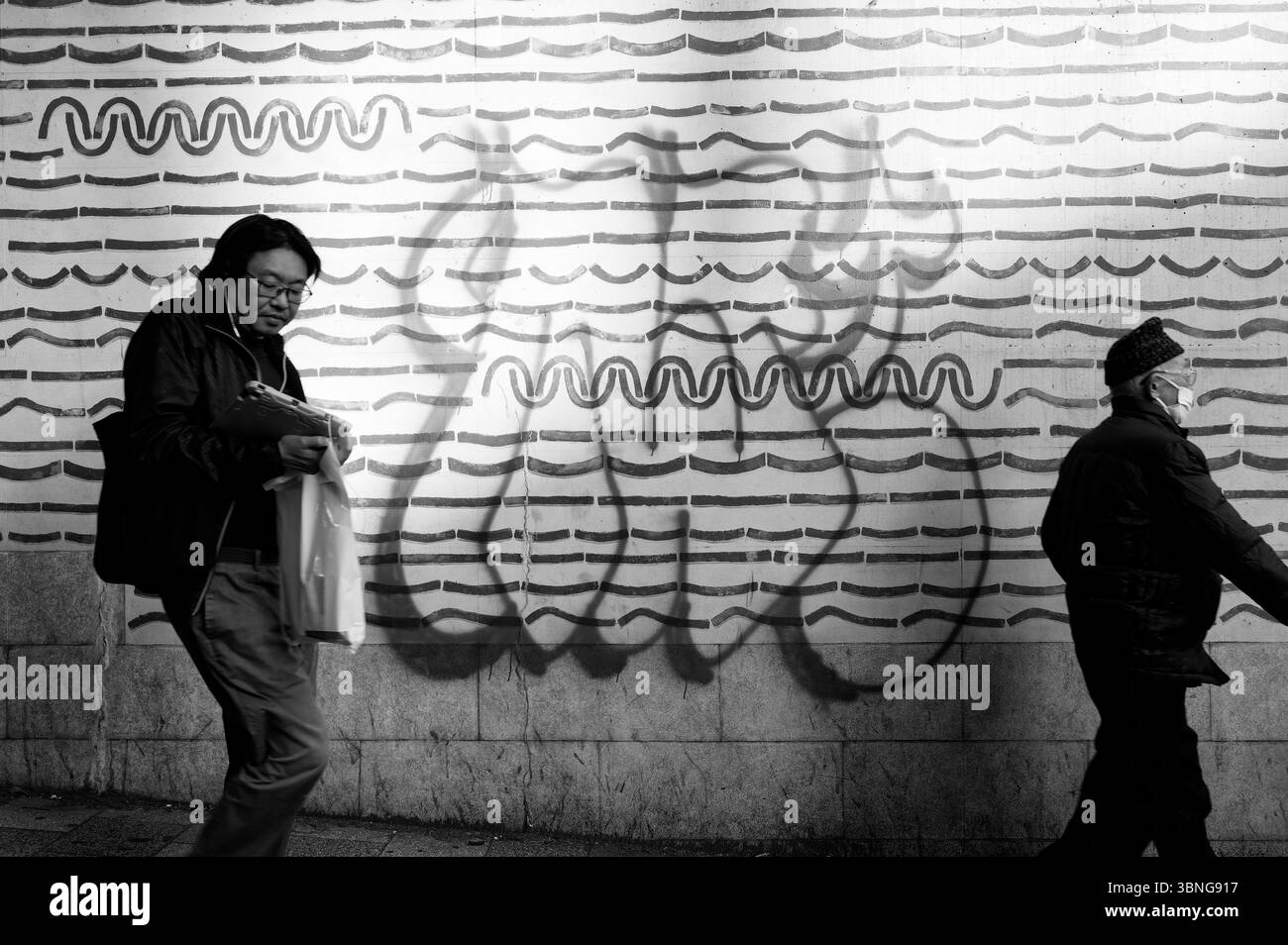 Scena di Tokyo in bianco e nero, con pedoni che camminano davanti a audaci linee d'arte e graffiti sbiaditi Foto Stock