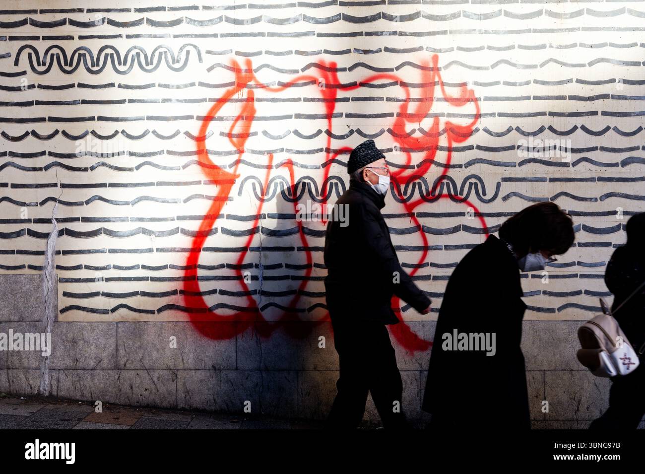 Il vecchio passeggia davanti a un muro di Tokyo ricoperto di opere d'arte in linea ondulata e audaci graffiti rossi Foto Stock