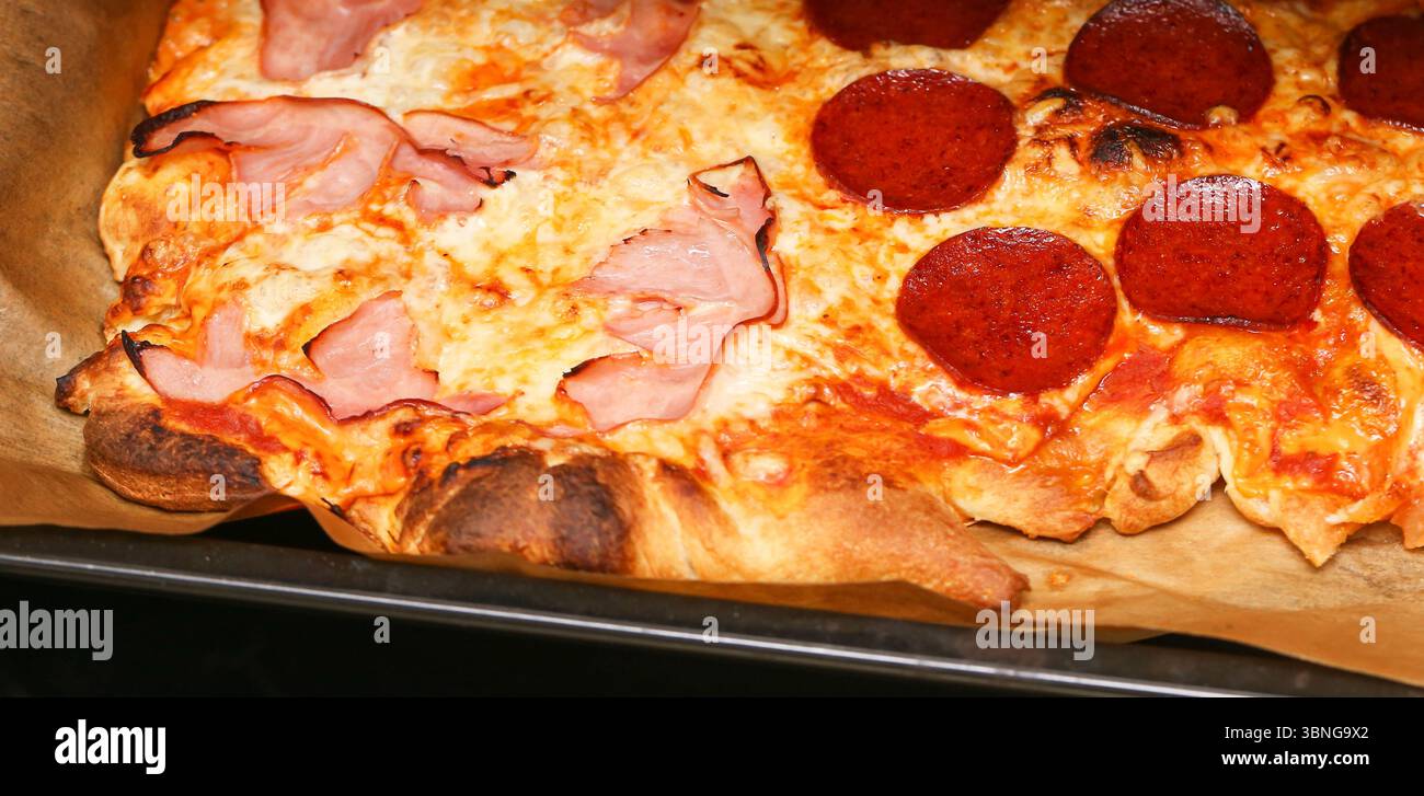Pizza calda al forno con formaggio fuso. Piatto italiano con condimenti di salame e prosciutto. Crosta croccante e superficie dorata. Delizioso cibo fatto in casa. Foto Stock
