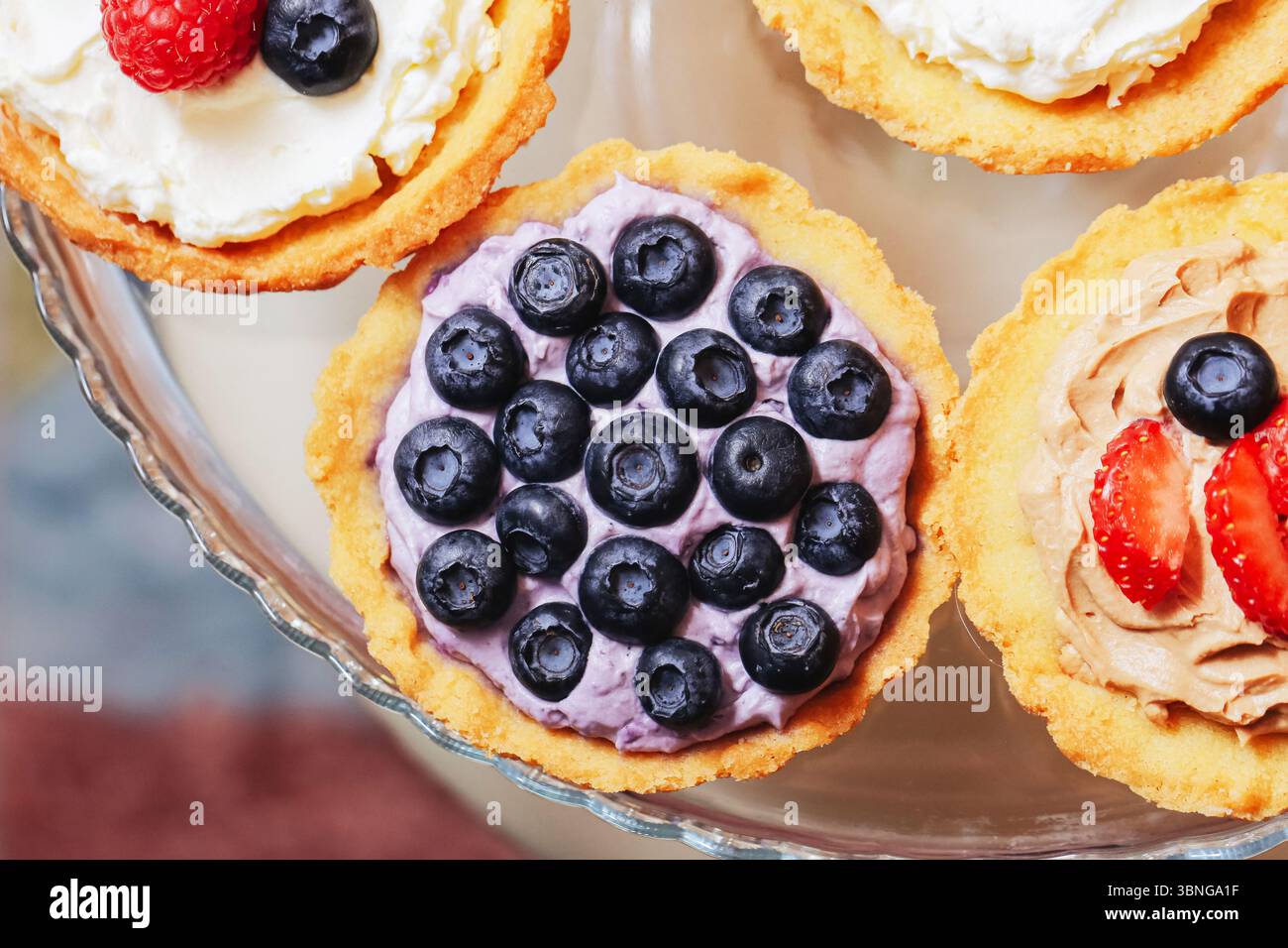 Crostate di bacche colorate. Mini torta di frutta con mirtilli e fragole. Delizioso dessert su piatto di vetro. Dolce estivo. Gourmet fatto in casa. Foto Stock