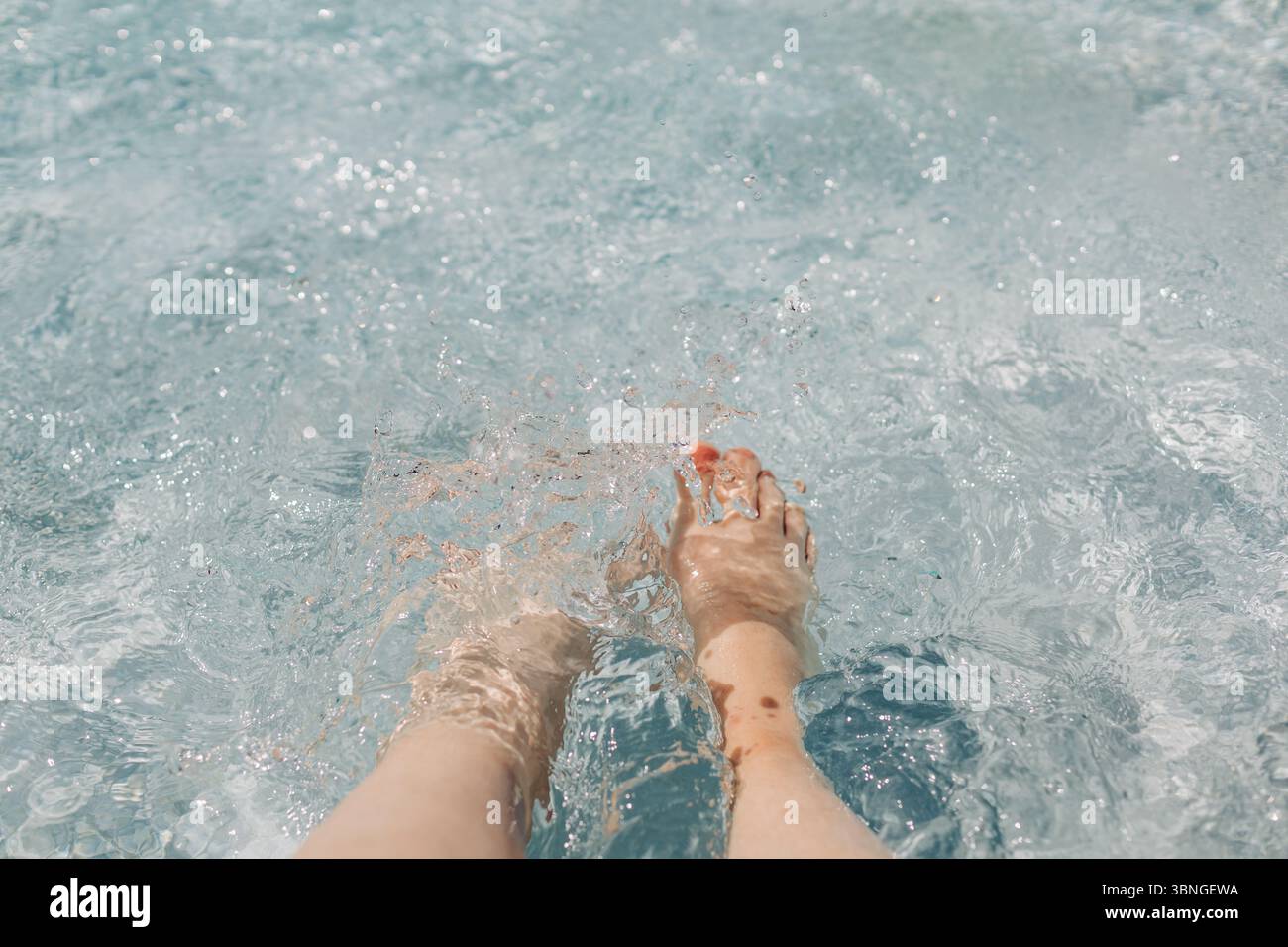 I piedi disturbano delicatamente l'acqua limpida di una piscina in un pomeriggio di sole, creando increspature e schizzi. Foto Stock