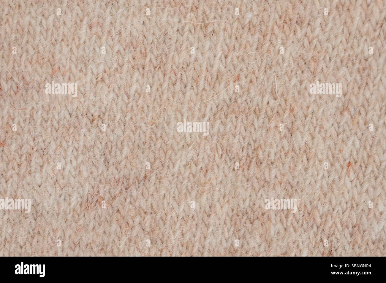 La vista ravvicinata mostra il tessuto lavorato a maglia con una texture morbida in calde tonalità beige, perfetto per l'abbigliamento e gli accessori invernali. Foto Stock