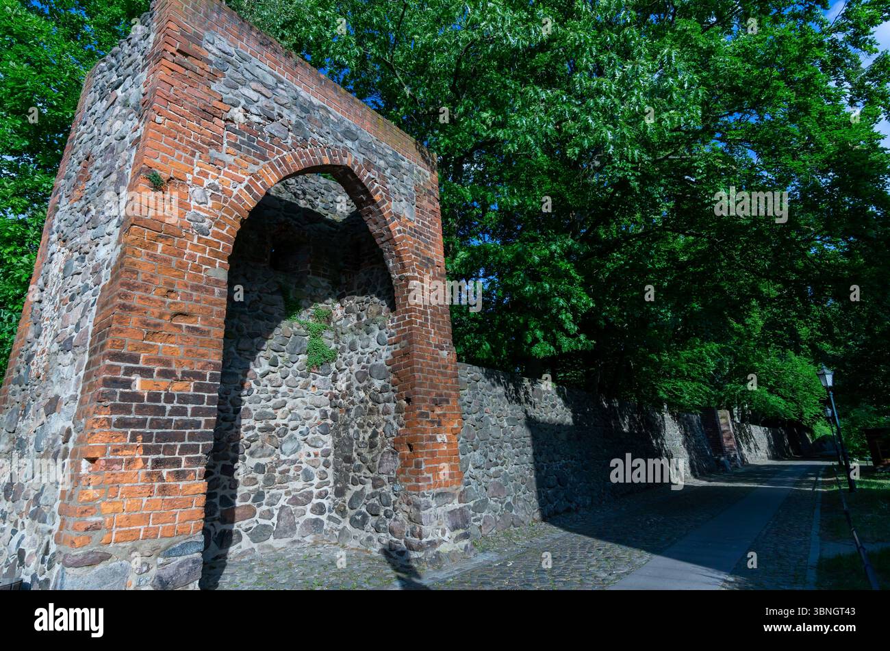 Storico muro in mattoni e pietra dalle fortificazioni medievali di Bernau bei Berlin, circondato da alberi e sentieri acciottolati. Foto Stock