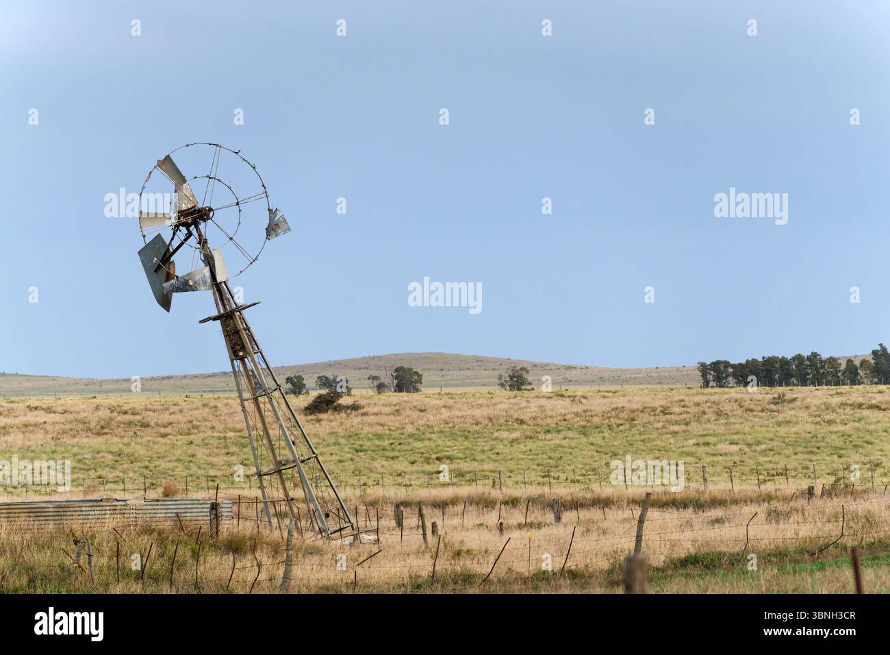 Mulino a vento danneggiato in un campo asciutto, che rappresenta il decadimento rurale e l'impatto della siccità sull'agricoltura Foto Stock