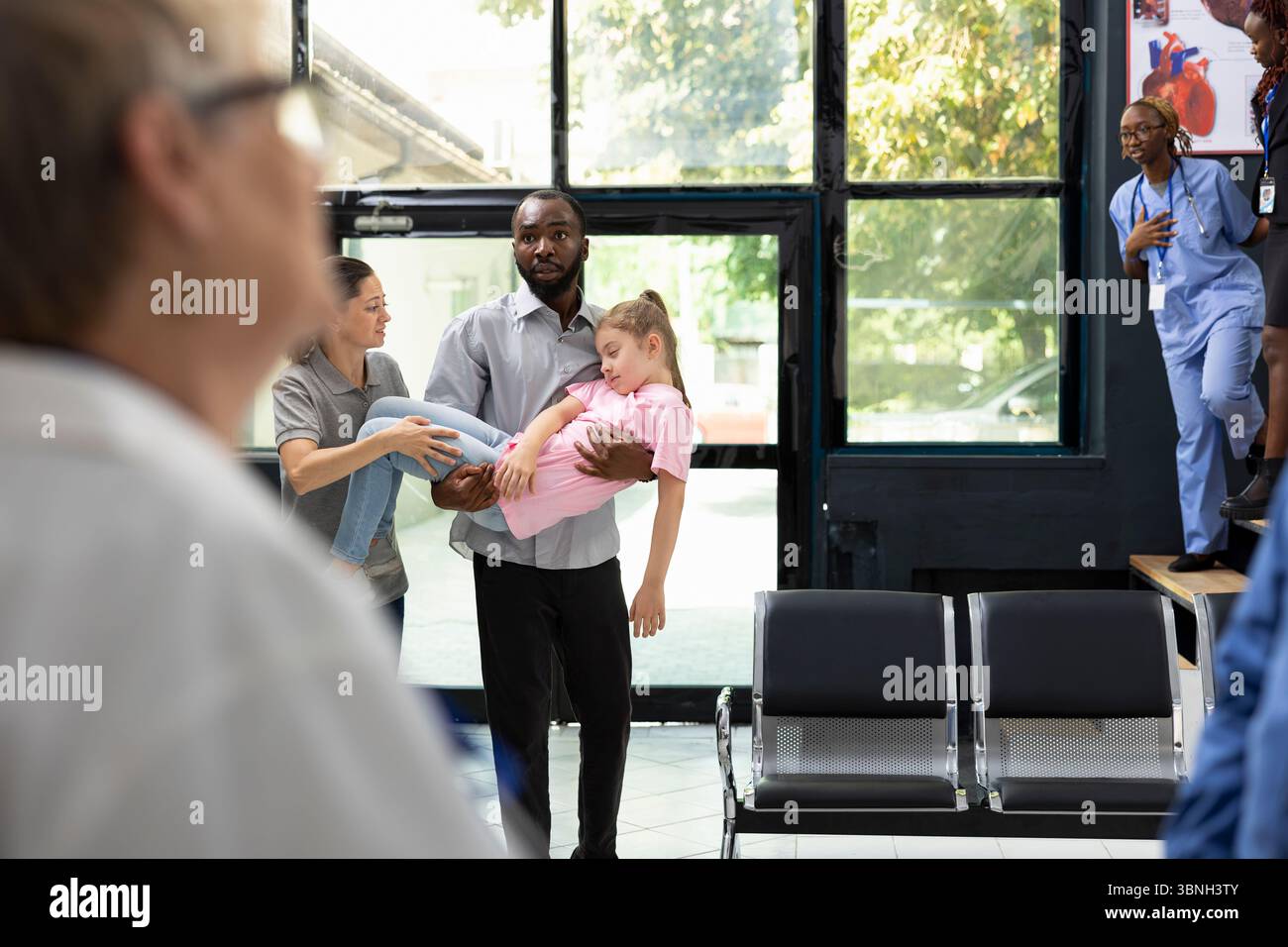 Ragazza svenuta e suo padre afroamericano la sta portando in ospedale, in attesa di risposta immediata da parte dell'equipe medica. Situazione clinica caratterizzata da urgenza e preoccupazione familiare. Foto Stock
