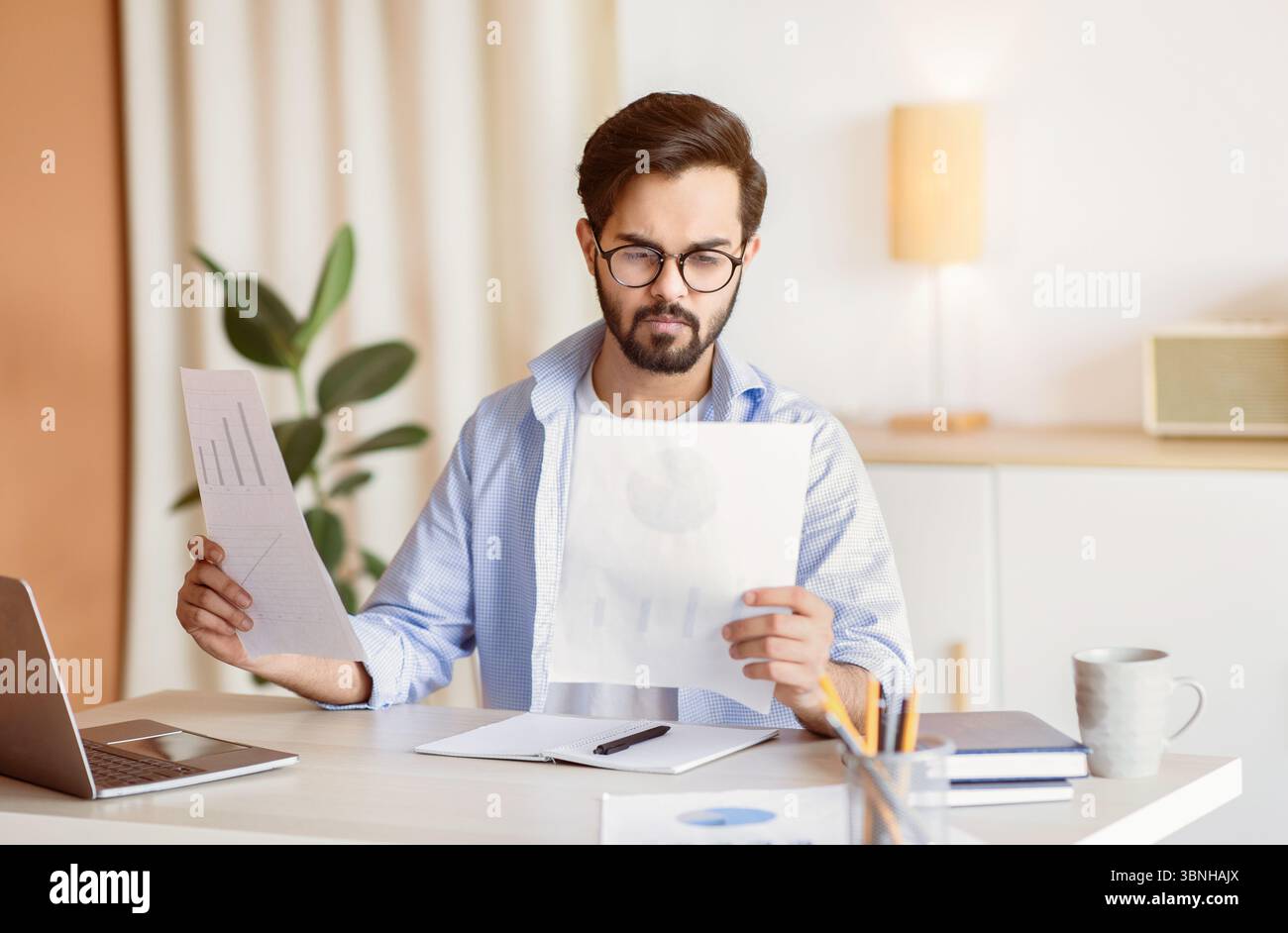 Bell'imprenditore orientale che legge i documenti finanziari mentre si siede alla scrivania In ufficio Foto Stock