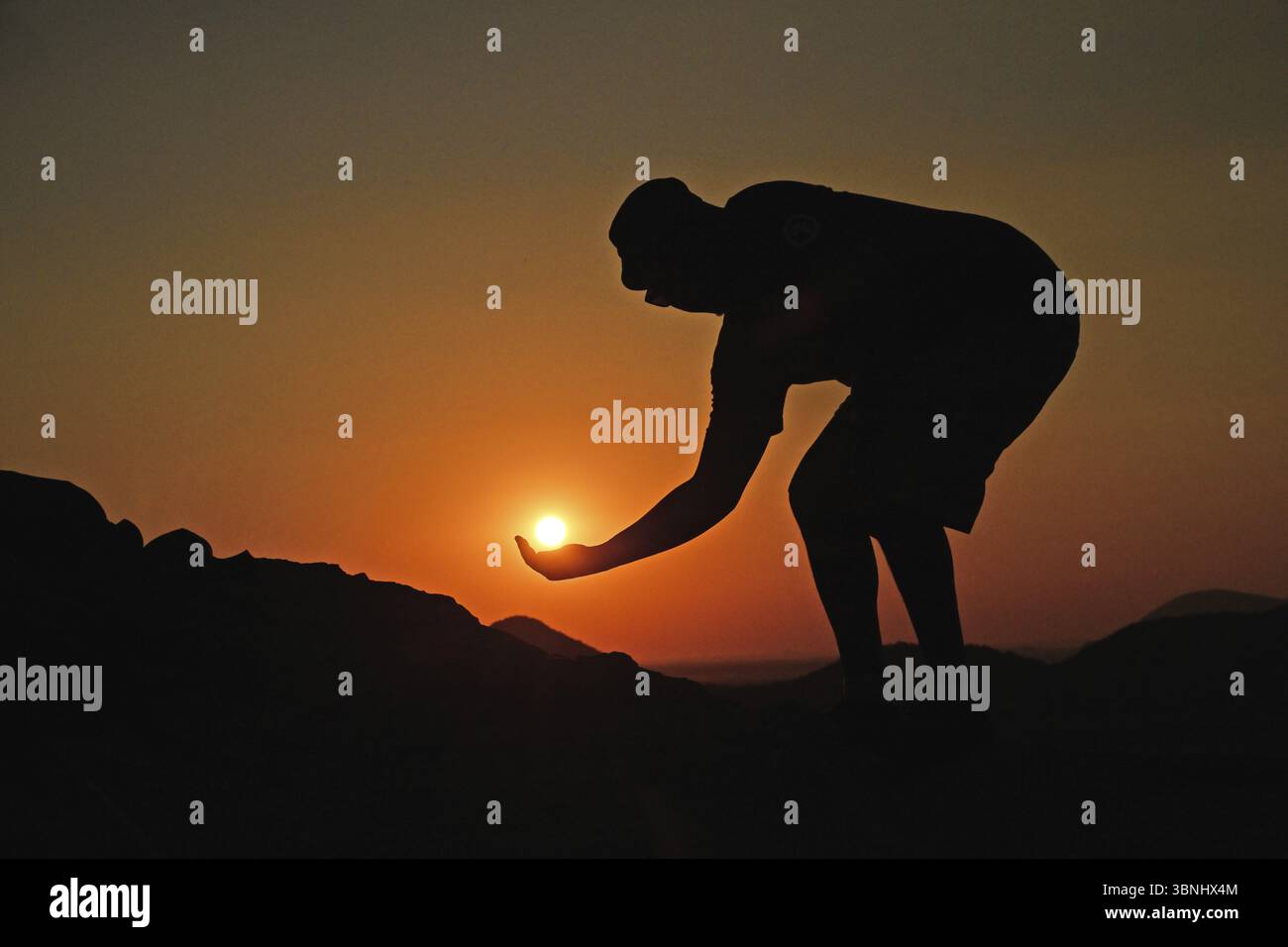 Un uomo sagomato tiene in mano il sole che tramonta, Namibia, Africa Foto Stock