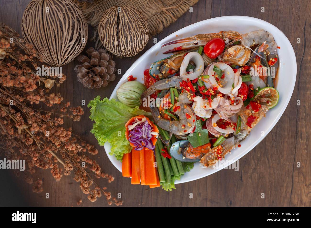 Una vista dall'alto di una colorata insalata di pesce speziata in stile thailandese servita su un piatto bianco. Il piatto è caratterizzato da un vivace mix di granchi, gamberi, cozze, capesante, ecc. Foto Stock