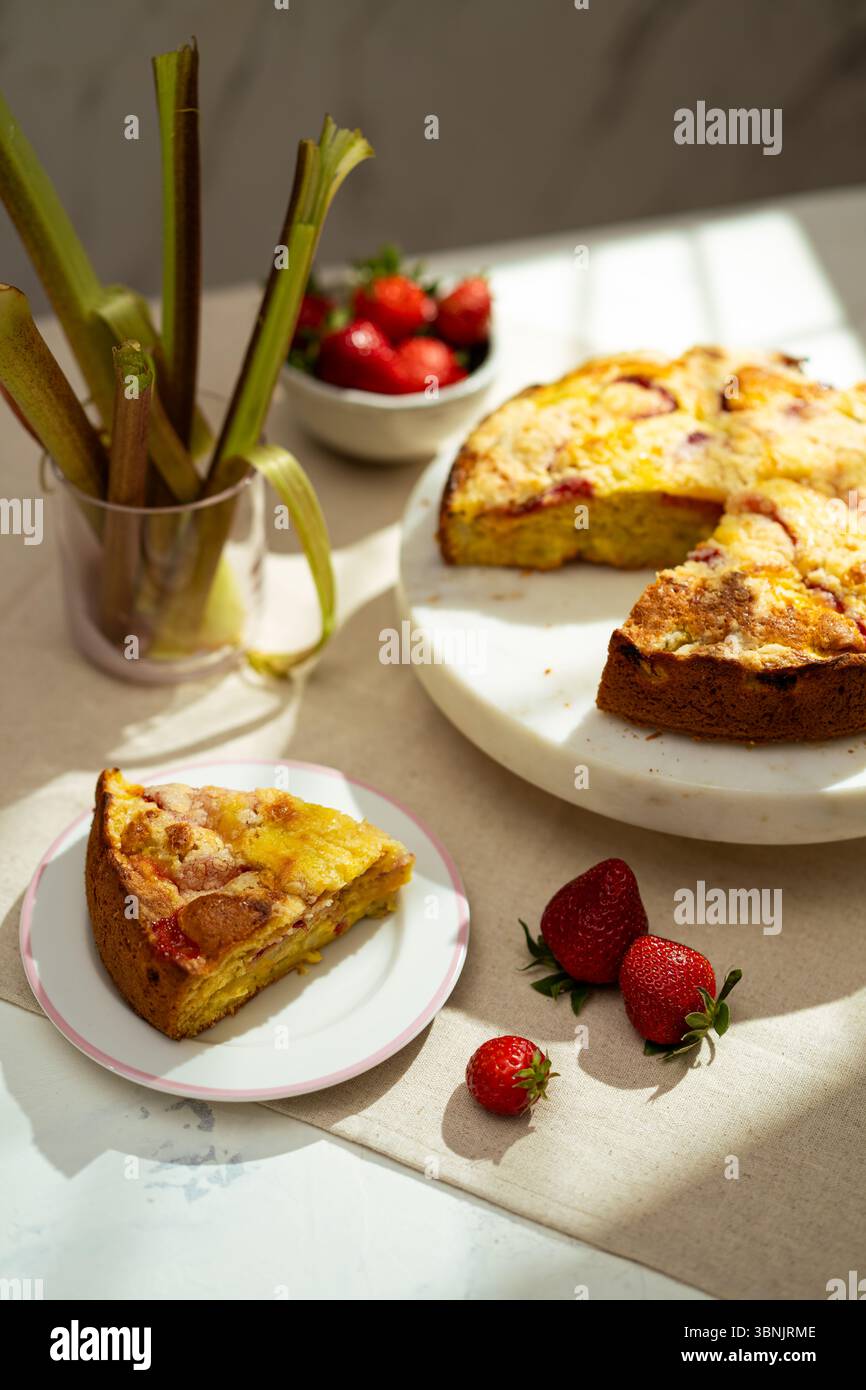 Deliziati con una torta di fragole al rabarbaro fatta in casa posta su un piatto di marmo bianco, che presenta fette vivaci e fragole fresche per una deliziosa somma Foto Stock