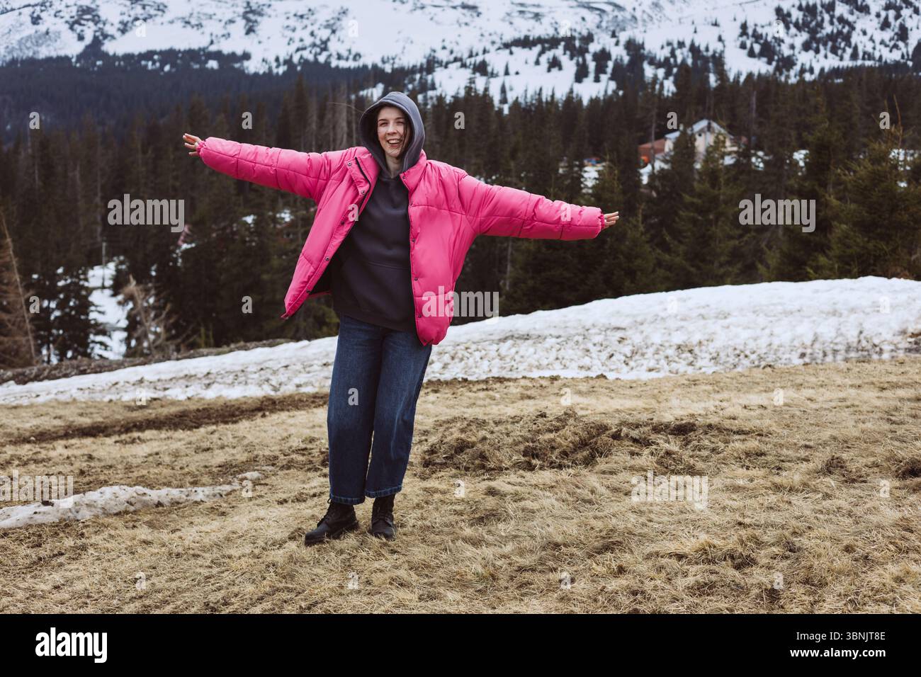 Una persona con una giacca rosa abbraccia con gioia il paesaggio innevato delle montagne. Circondati da alberi e neve, godono di un momento rinfrescante e tranquillo Foto Stock