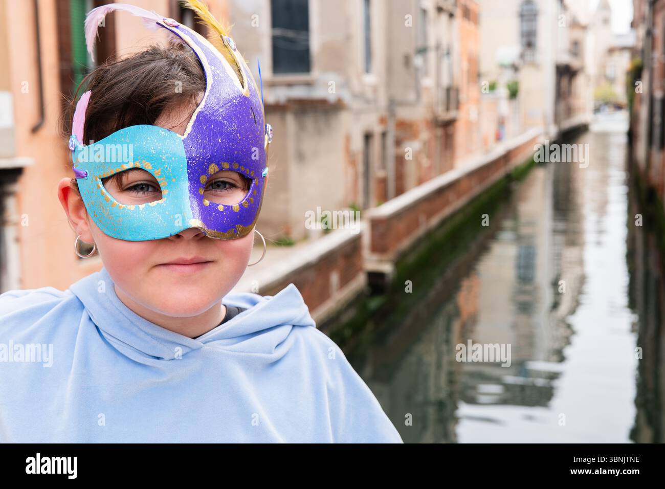 Un bambino che indossa una colorata maschera di carnevale a Venezia, Italia. La vivace maschera sfoggia il tradizionale design veneziano, catturando lo spirito festivo del Foto Stock