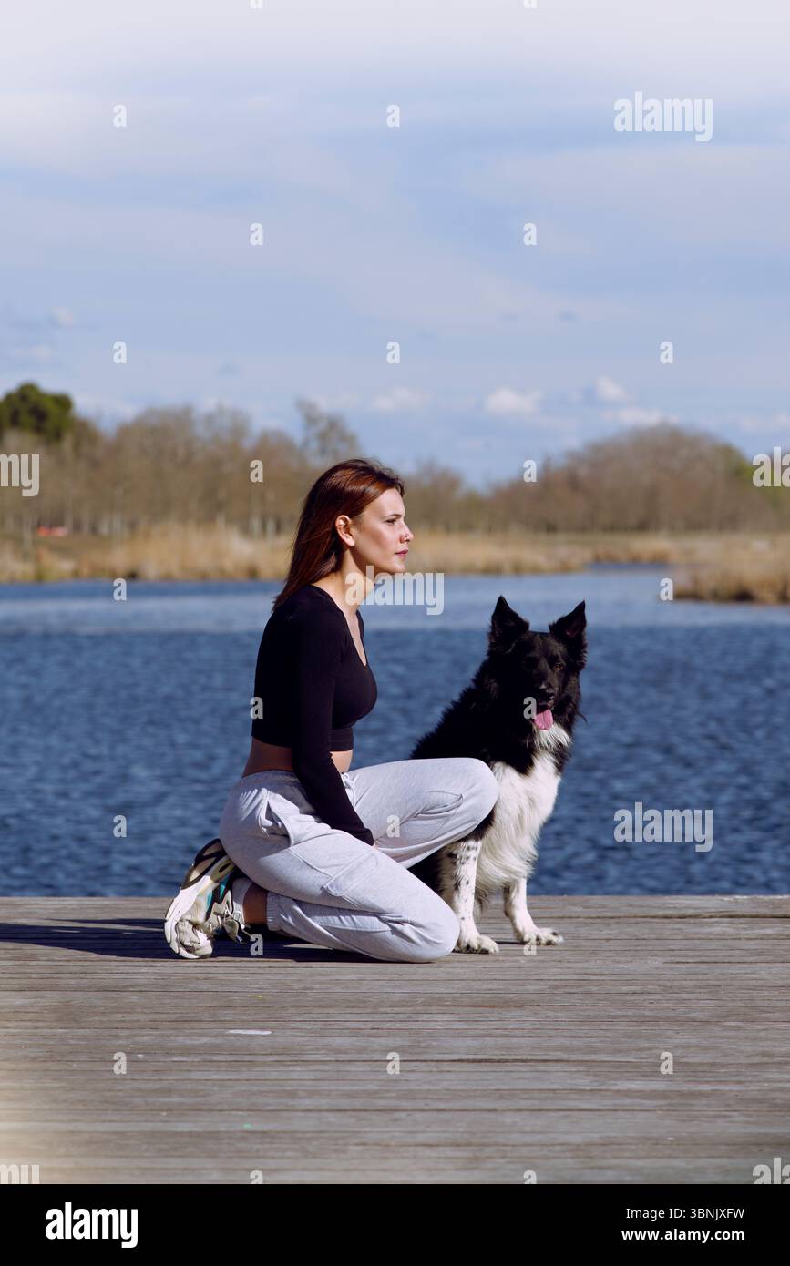 Una donna trascorre un pomeriggio sereno al lago con il suo cane, godendosi la tranquillità della natura. Il legame tra di loro è evidente in quanto condividono un silenzio Foto Stock