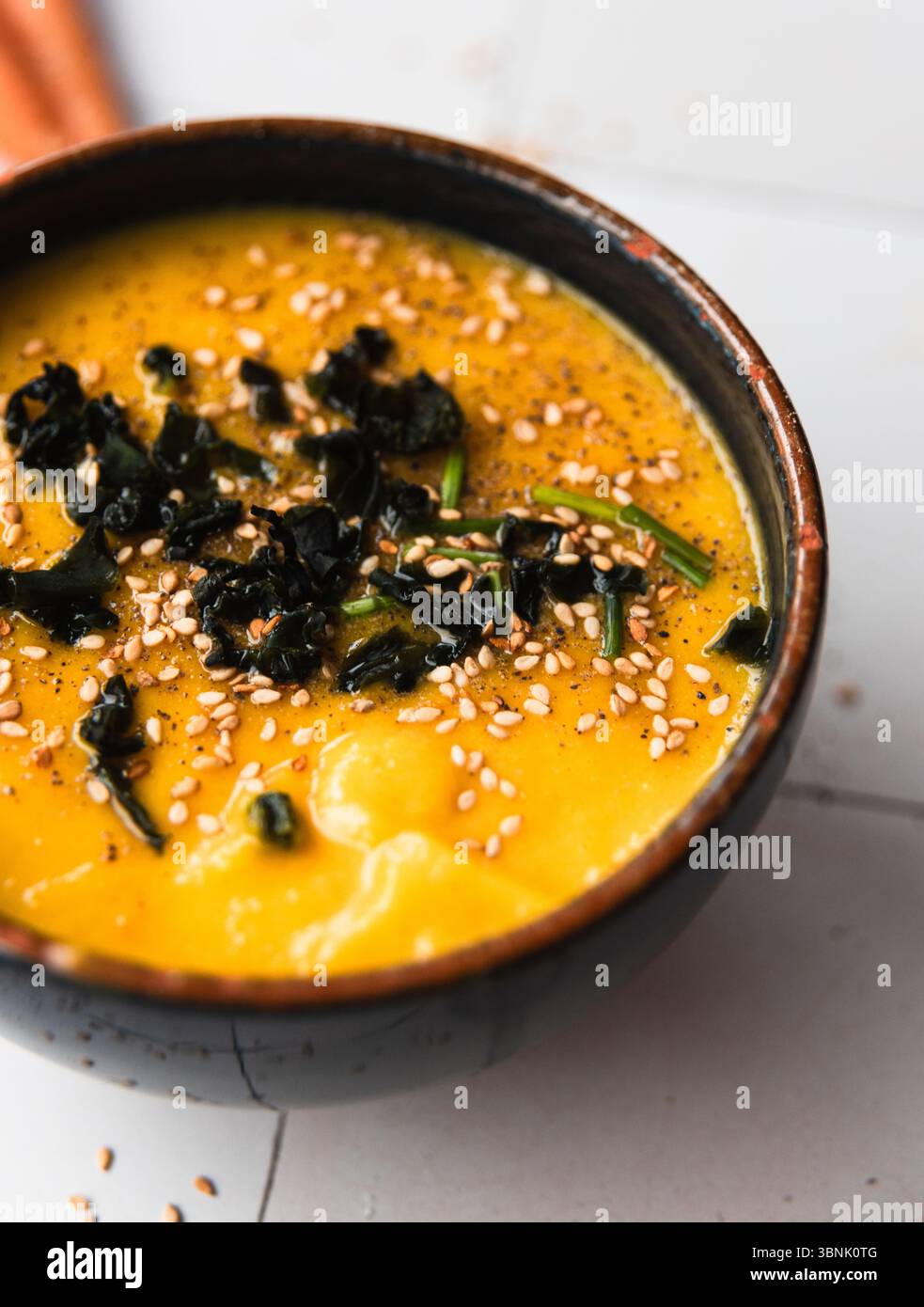 Una calda e invitante ciotola di zuppa di crema di zucca guarnita con delicate alghe wakame e cosparsa di semi di sesamo. Perfetto per un pasto accogliente, per catturare Foto Stock
