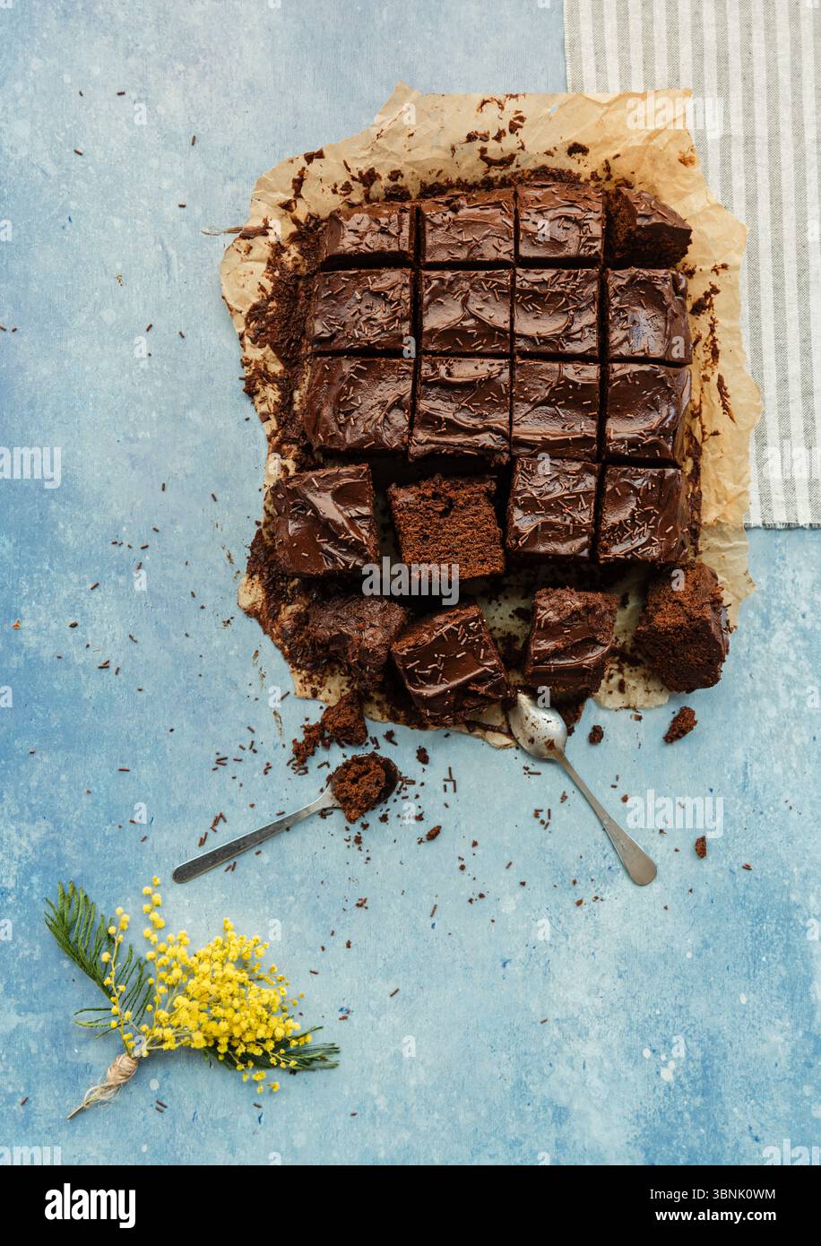 Una ricca torta al cioccolato è presentata elegantemente su uno sfondo marrone rustico, impreziosita da vibranti fiori gialli, creando un aspetto armonioso e invitante Foto Stock