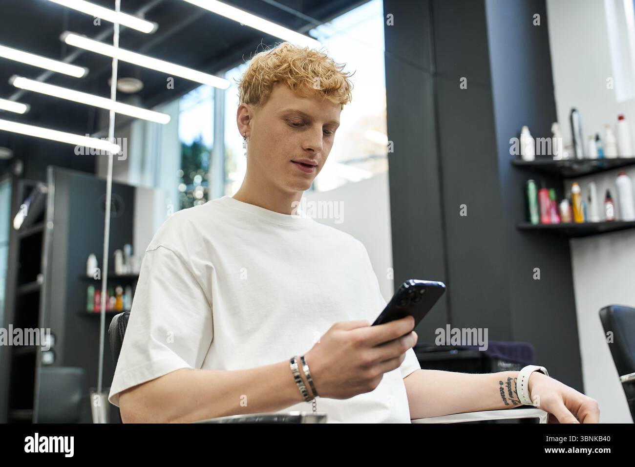 Il cliente si rilassa in un elegante salone di bellezza, sfogliando le ultime tendenze della moda su uno smartphone. Foto Stock