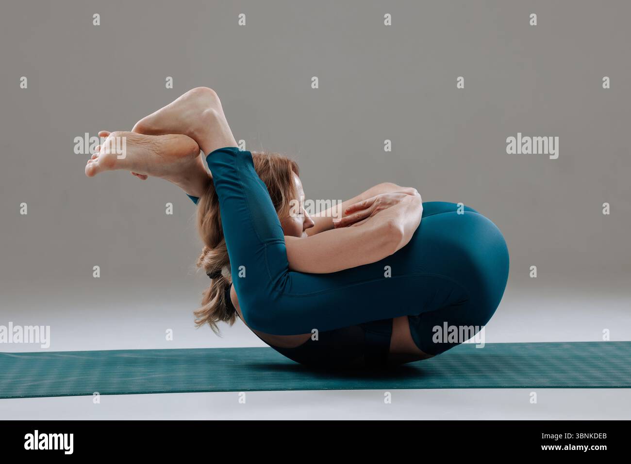 Donna flessibile che esegue yoga avanzato si piega in posa all'interno, mostrando forza, benessere e profonda consapevolezza del corpo Foto Stock