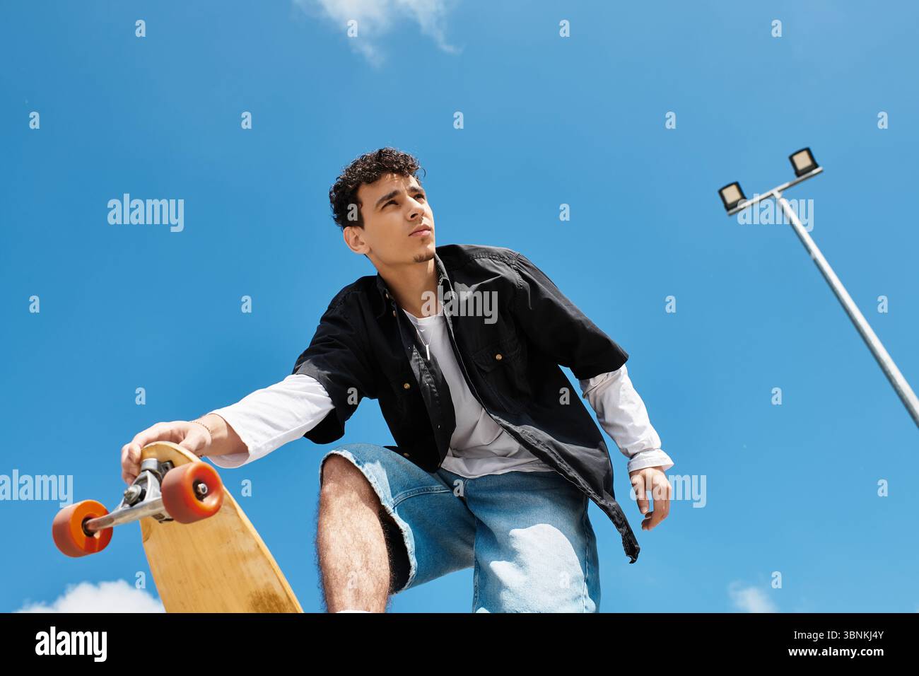 Un giovane ragazzo si bilancia sapientemente sullo skateboard mentre si gode la giornata di sole nel parco. Foto Stock