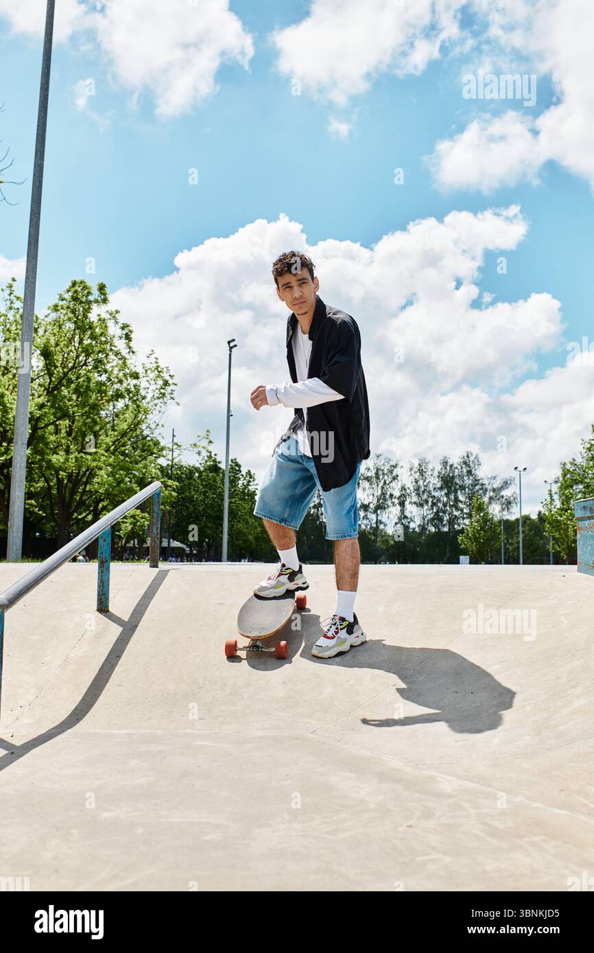 Un giovane skateboard sapientemente nel parco sotto un cielo azzurro con nuvole. Foto Stock