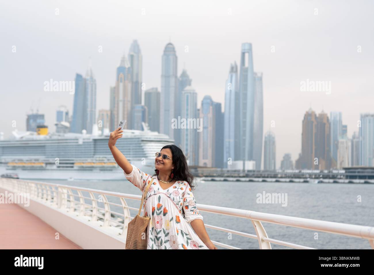 Sfondo di Dubai Marina con crociera in barca a vela nel mare e una giovane donna turistica che scatta foto, viaggi di lusso a Dubai e foto di scorta di stile di vita Foto Stock