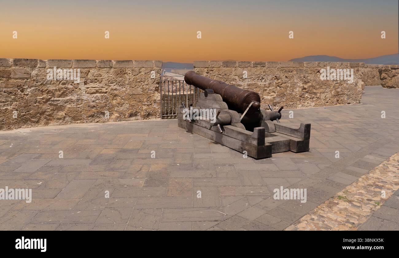 Cannone storico sulle mura fortificate di Alghero, con il cielo del tramonto sullo sfondo Foto Stock