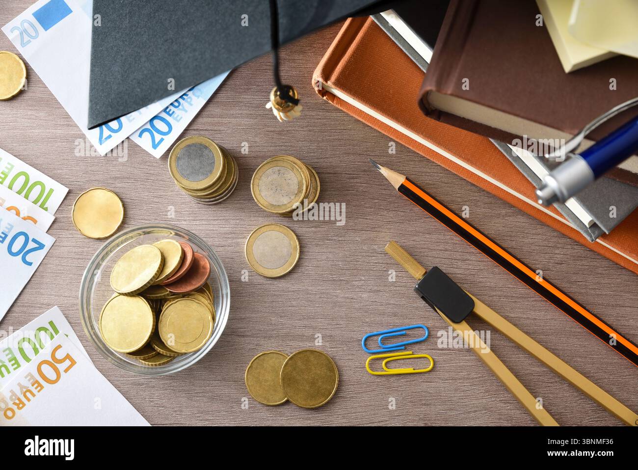 Dettaglio del concetto di spesa per l'istruzione con bacheca su una pila di libri e denaro su un tavolo di legno. Vista dall'alto. Foto Stock