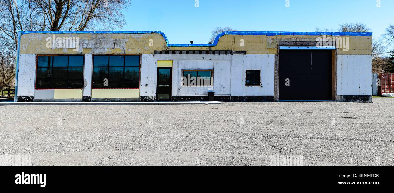 vista frontale panoramica di una stazione di benzina d'epoca e garage in fase di ristrutturazione con parcheggio in ghiaia e cielo blu Foto Stock
