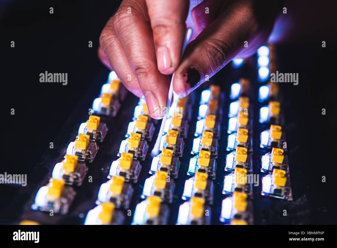Primo piano di una persona che pulisce gli interruttori meccanici gialli della tastiera utilizzando un cotton fioc. Foto Stock