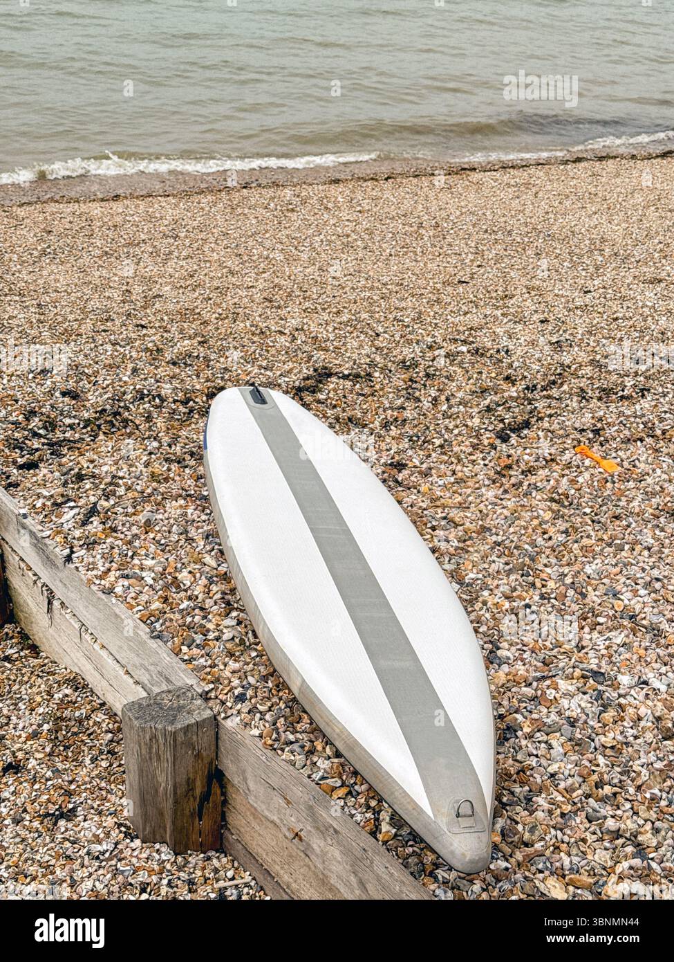 Paddleboard adagiato su una spiaggia di scisto. Niente persone. - Immagine stock catturata con smartphone