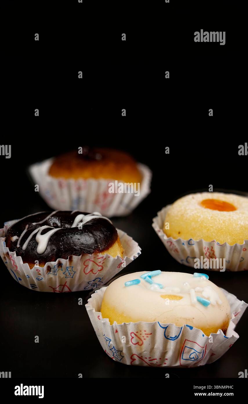 Piccole ciambelle di vari gusti su sfondo nero. Foto Stock