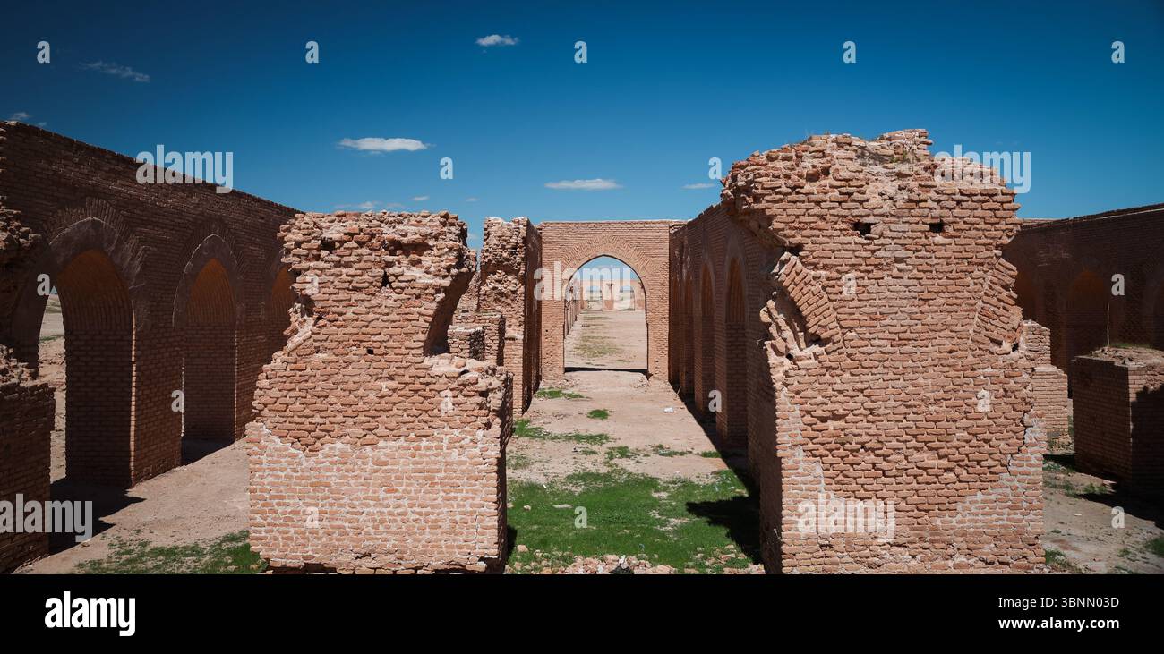 Le rovine di un'antica struttura ad Abu Dulaf mostrano archi in mattoni e resti di architettura storica contro un cielo vibrante. Foto Stock