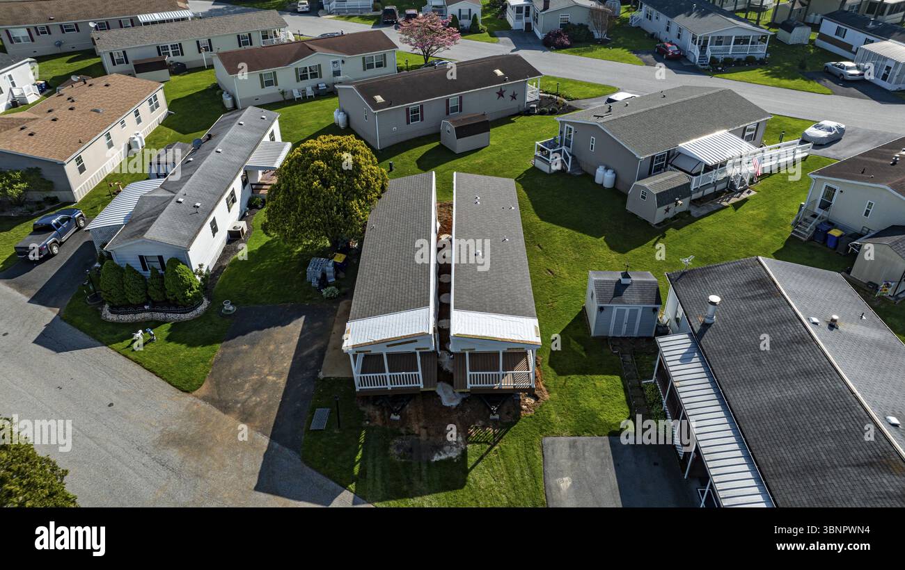 La vista aerea mostra le case mobili costruite lungo una strada tranquilla, circondate da prati e alberi ben tenuti. Il sole emette una luce calda Foto Stock