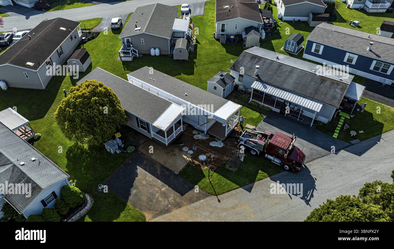 La vista aerea mostra le case mobili costruite lungo una strada tranquilla, circondate da prati e alberi ben tenuti. Il sole emette una luce calda Foto Stock