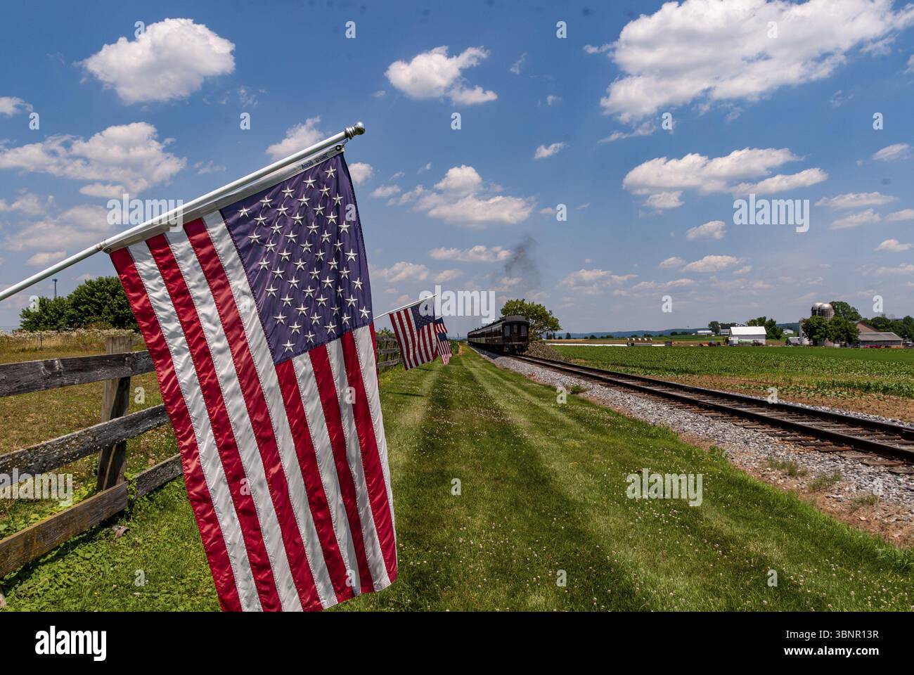 Veduta delle Bandiere americane che sventolano su una recinzione dopo che un treno passeggeri a vapore è passato in una soleggiata giornata estiva Foto Stock