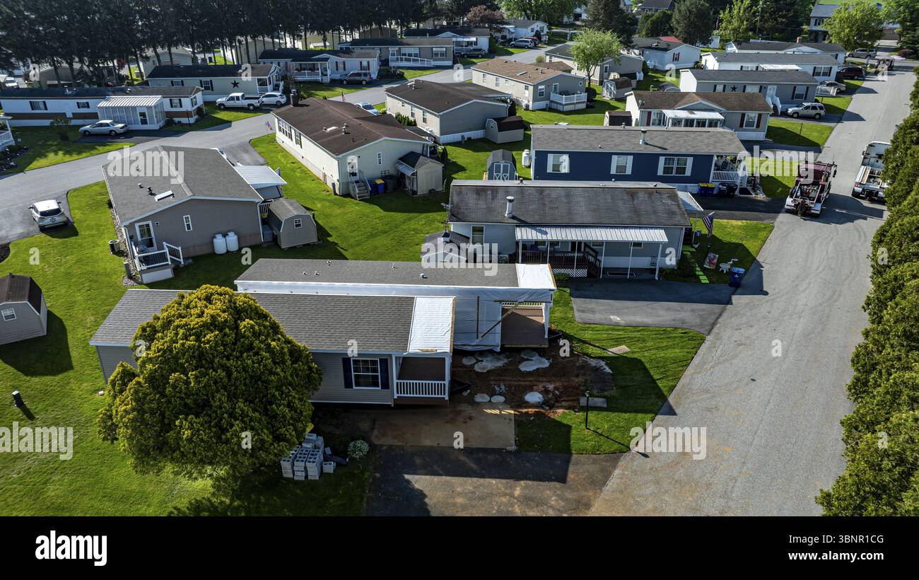 La vista aerea mostra le case mobili costruite lungo una strada tranquilla, circondate da prati e alberi ben tenuti. Il sole emette una luce calda Foto Stock