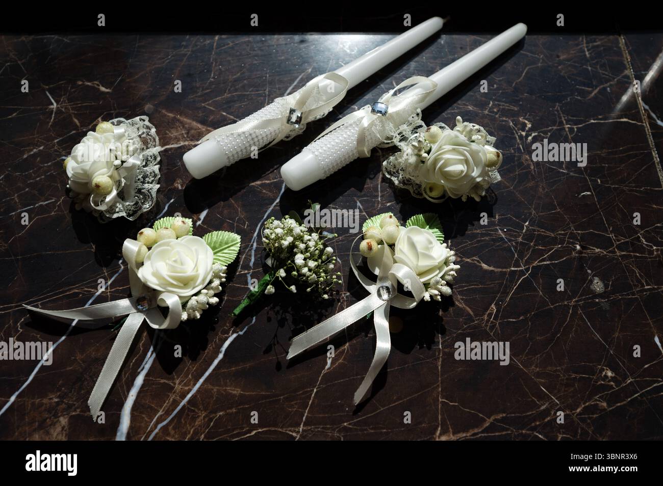 Le candele a cono bianco adornate con perle e nastri, accompagnate da delicate boccali di rose bianche, creano un raffinato dettaglio per il matrimonio. Gli oggetti riposano Foto Stock