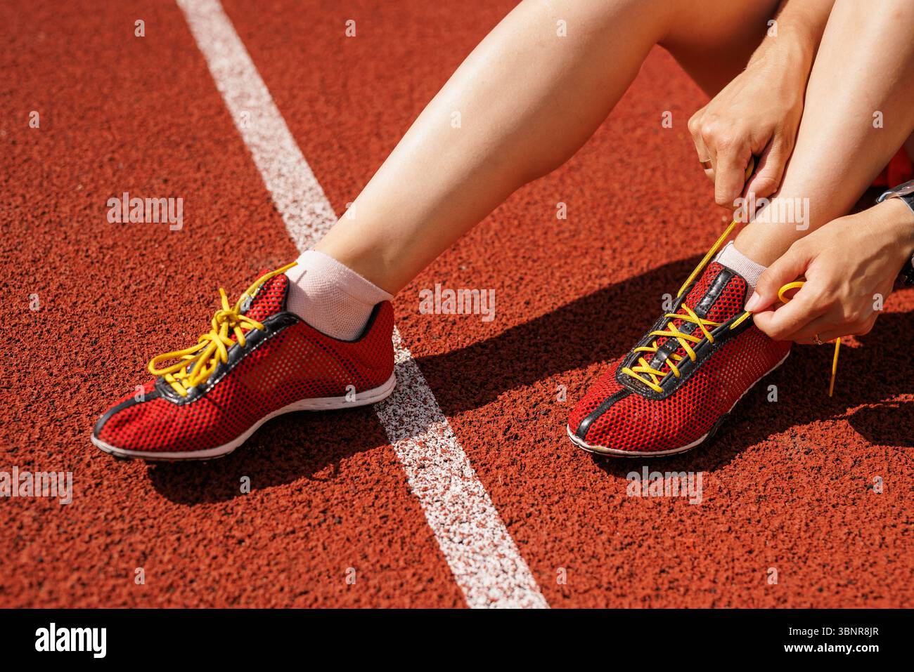 Primo piano dell'atleta che lega scarpe sulla pista da corsa rossa preparandosi per l'allenamento all'aperto fitness e uno stile di vita sano. Foto Stock