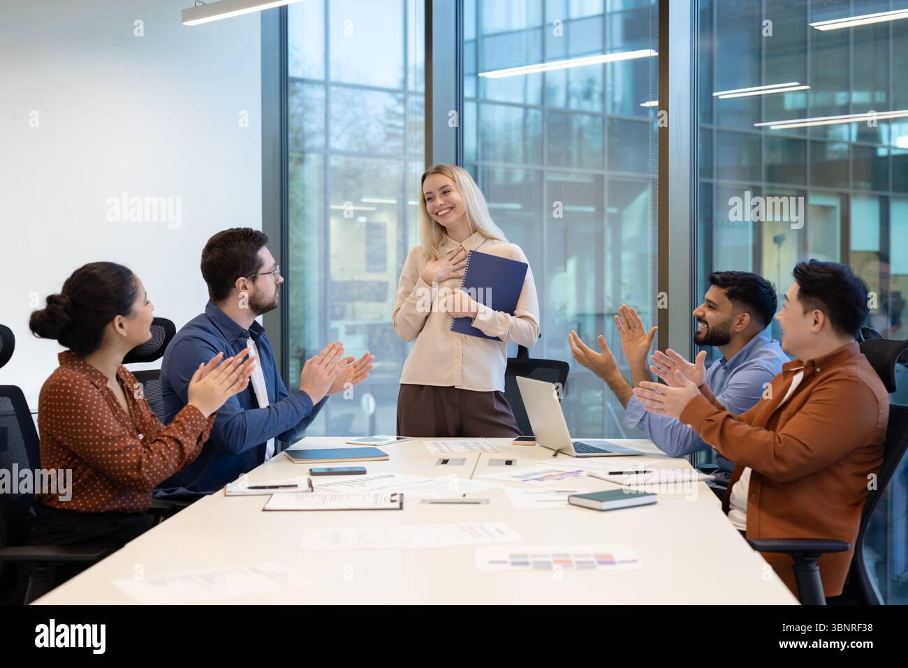 Un team eterogeneo applaude il collega in un ufficio, celebrando il successo e il lavoro di squadra. Foto Stock