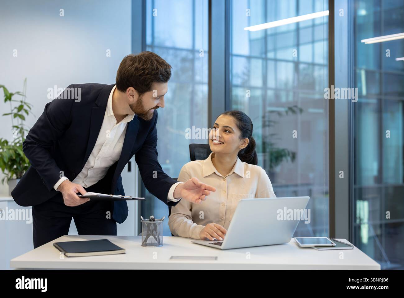 Un uomo d'affari guida e consiglia una donna d'affari mentre lavora su un notebook in un ufficio moderno. Foto Stock