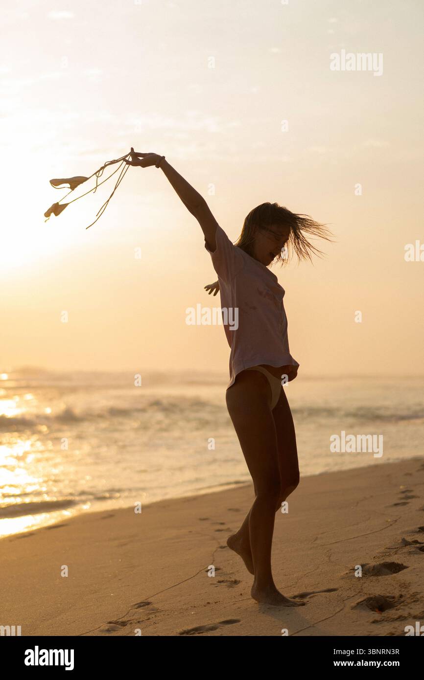 Donna che balla sulla spiaggia al tramonto girando il costume da bagno al vento Foto Stock
