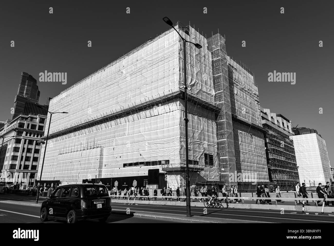 Regno Unito, Londra, 07 luglio 2025. Un grande edificio in fase di ristrutturazione avvolto da impalcature e lenzuola bianche vicino al London Bridge, con pedoni Foto Stock