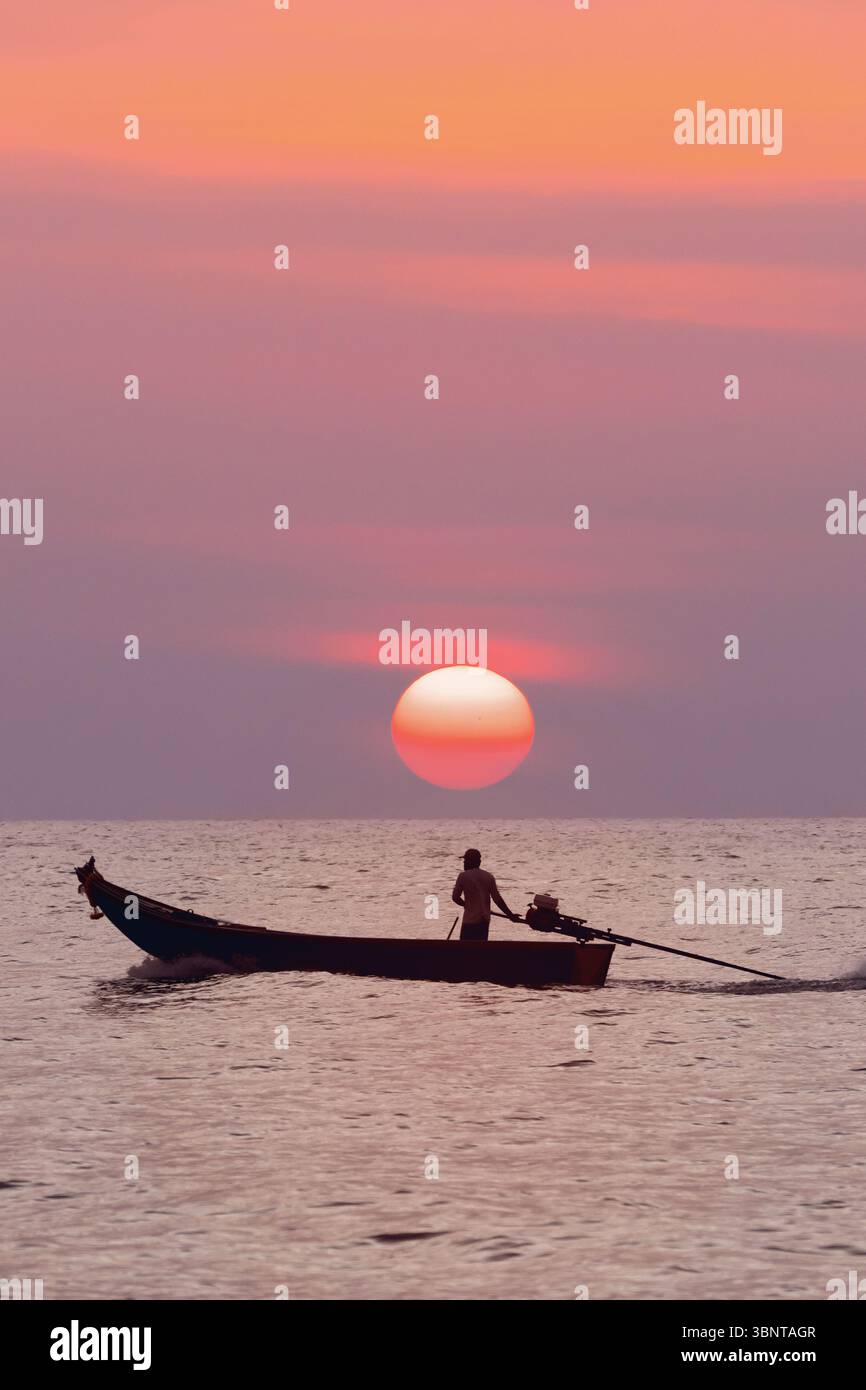 Un pescatore solitario su una tradizionale barca a coda lunga tailandese che naviga sul mare sotto il sole arancione che tramonta. Il concetto di marketing per viaggi ed escursioni Foto Stock