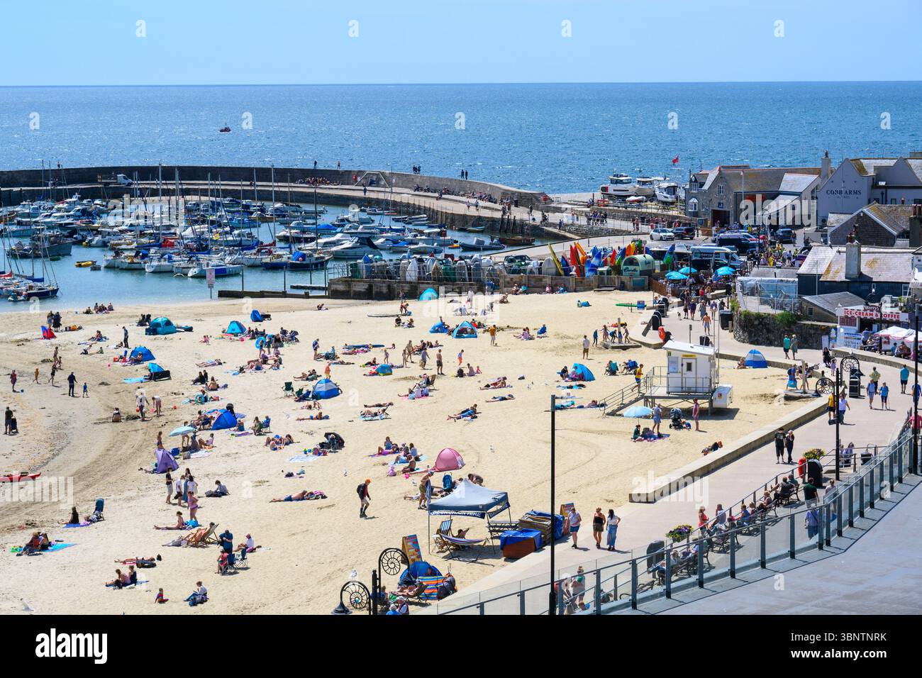 Lyme Regis, Dorset, Regno Unito. 4 luglio 2025. Meteo nel Regno Unito. I visitatori e la gente del posto si immergono nel caldo sole nella località balneare di Lyme Regis il venerdì. Le persone hanno sfruttato al meglio il tempo meraviglioso prima delle condizioni fredde e umide previste nel fine settimana. Il clima mite estivo tornerà la prossima settimana. Crediti: Celia McMahon/Alamy Live News Foto Stock