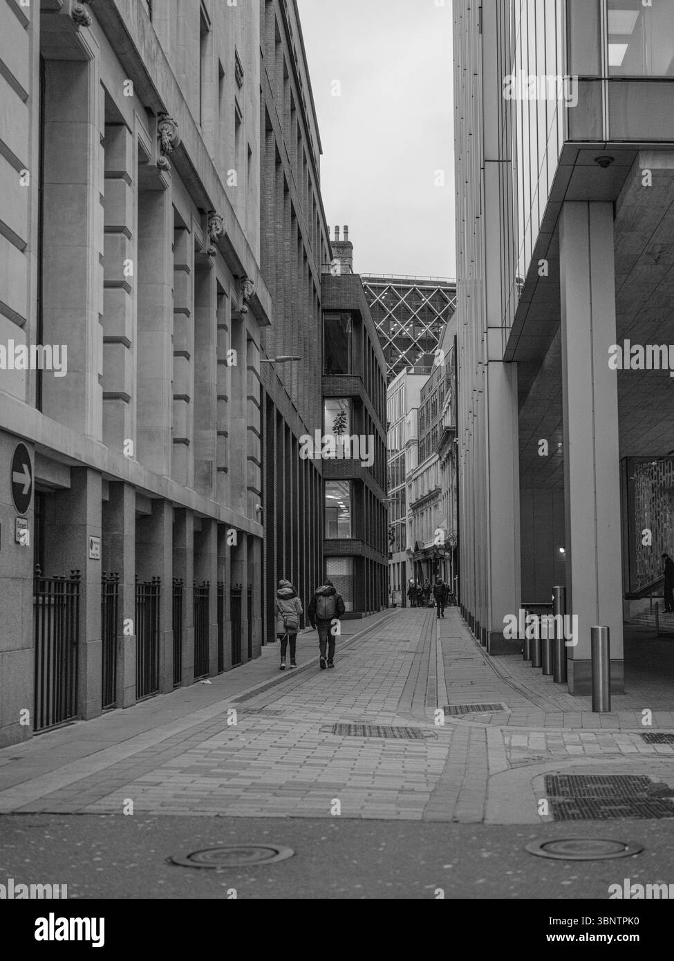 Regno Unito, Londra, 11 dicembre 2024. Vicolo stretto nel quartiere finanziario con un solitario pedonale tra alti edifici di uffici Foto Stock