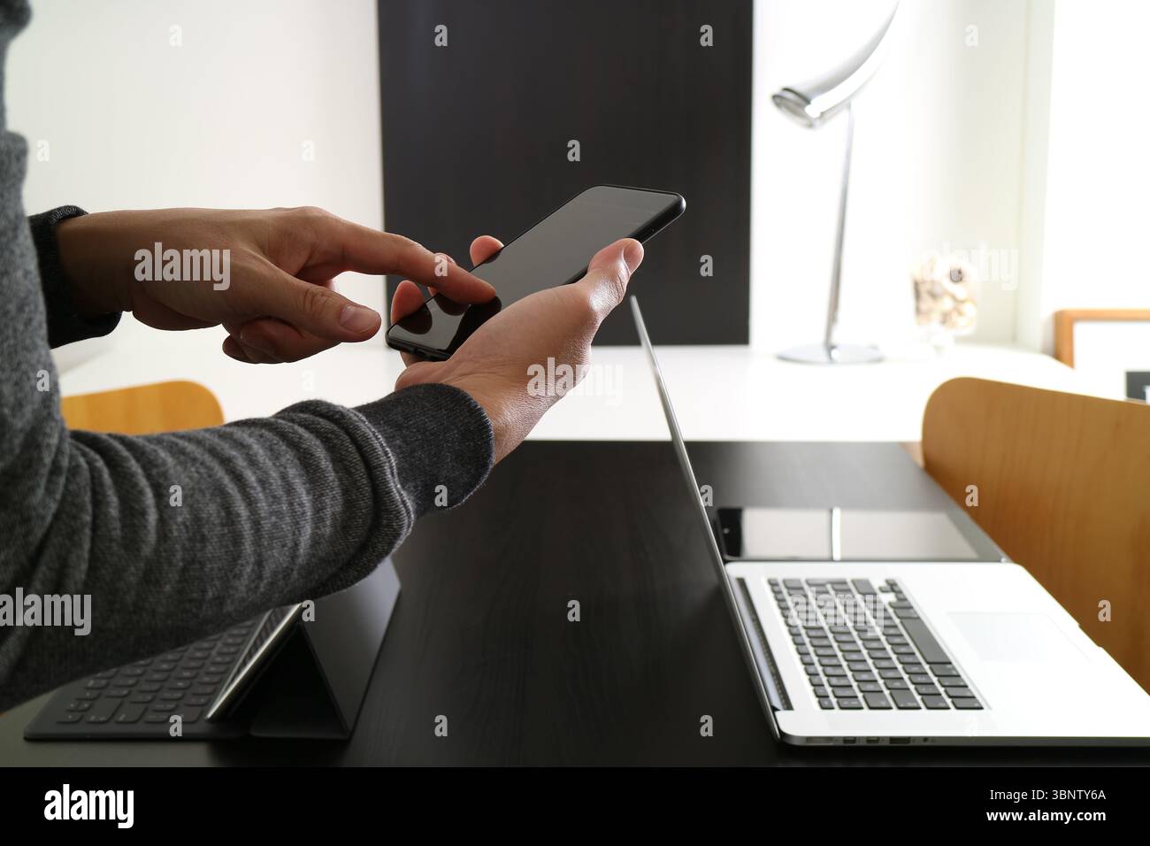 Immagine ravvicinata di una persona che utilizza uno smartphone in un ufficio moderno. Lo sfondo include un notebook e un tablet con tastiera, enfatizzazioni Foto Stock