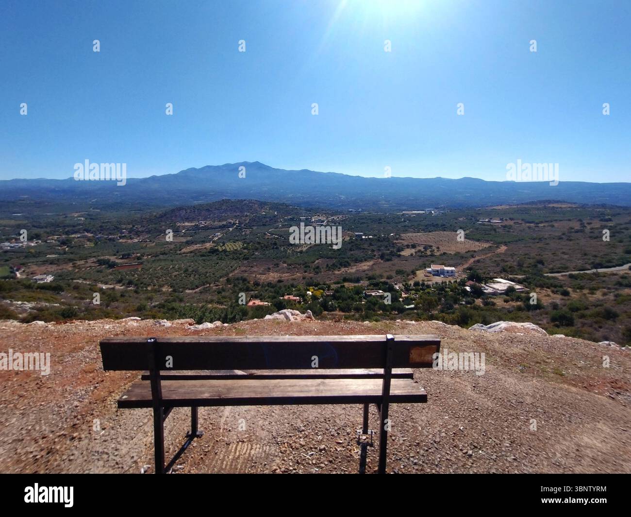 Una panchina di legno si affaccia su un paesaggio panoramico della valle e su montagne lontane sotto un cielo azzurro e limpido a Creta, in Grecia. Foto Stock
